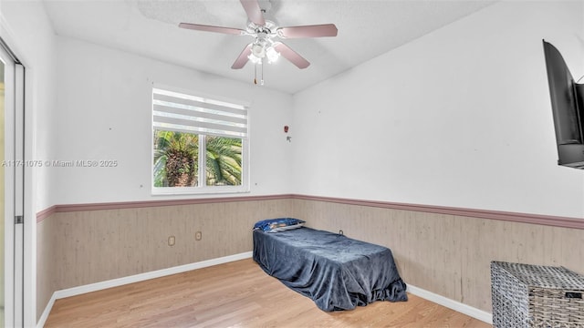 bedroom featuring hardwood / wood-style floors, ceiling fan, and wood walls