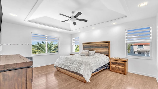 bedroom with a tray ceiling, light hardwood / wood-style flooring, and ceiling fan