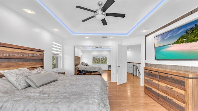 bedroom featuring a raised ceiling, ceiling fan, and light wood-type flooring