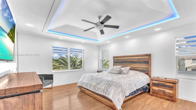 bedroom with ceiling fan, a raised ceiling, and light hardwood / wood-style flooring