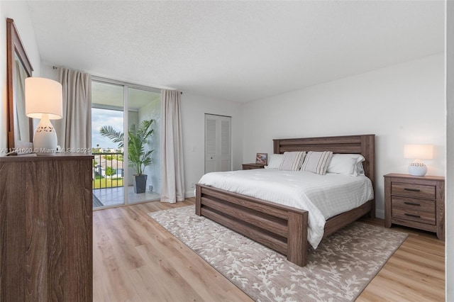 bedroom featuring expansive windows, access to outside, light hardwood / wood-style floors, a textured ceiling, and a closet