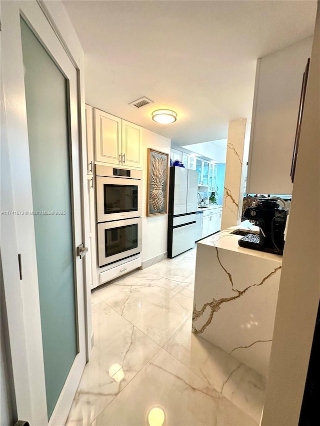 kitchen with white refrigerator, white cabinetry, stainless steel double oven, and light stone countertops