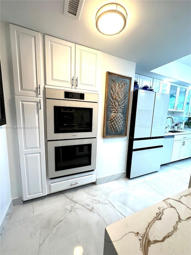 kitchen with light stone counters, white cabinetry, double wall oven, and refrigerator