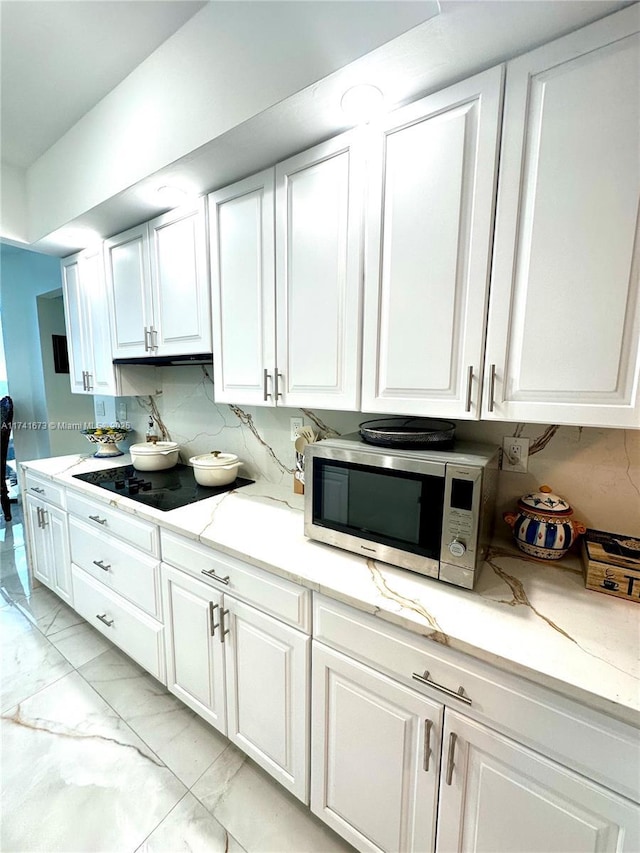 kitchen featuring black electric cooktop, light stone counters, decorative backsplash, and white cabinets