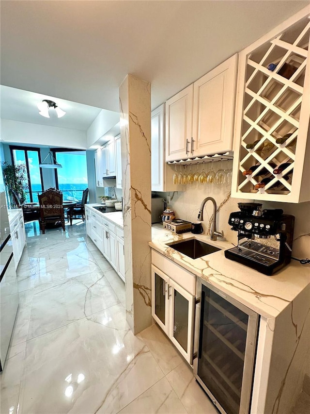 kitchen with sink, white cabinets, beverage cooler, backsplash, and light stone countertops