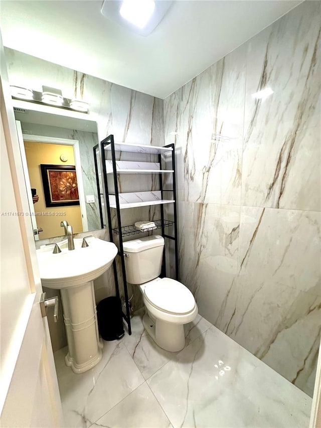 bathroom with toilet, sink, and tile walls