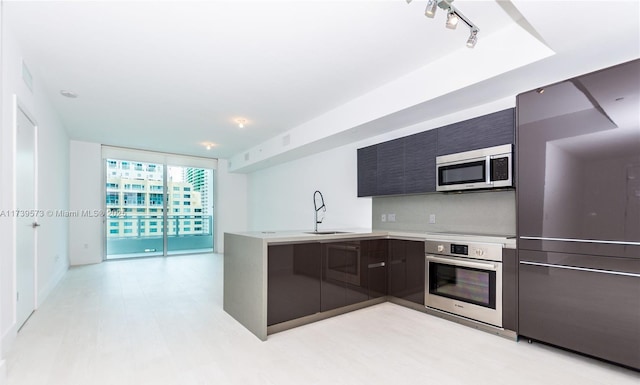 kitchen with sink, rail lighting, appliances with stainless steel finishes, kitchen peninsula, and light wood-type flooring