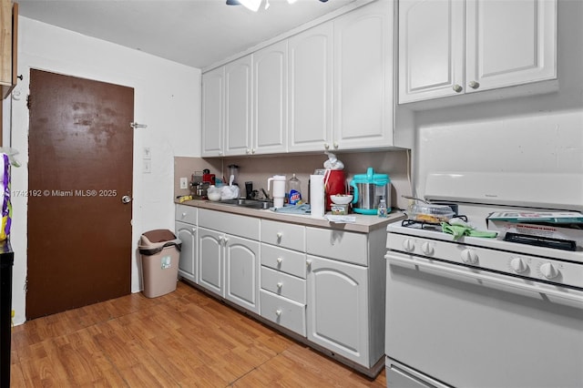 kitchen with white gas range, light hardwood / wood-style flooring, sink, and white cabinets