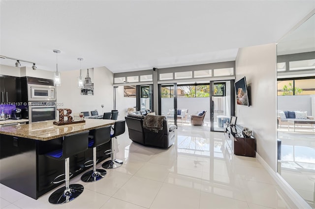 kitchen featuring pendant lighting, light tile patterned floors, a breakfast bar, appliances with stainless steel finishes, and light stone countertops