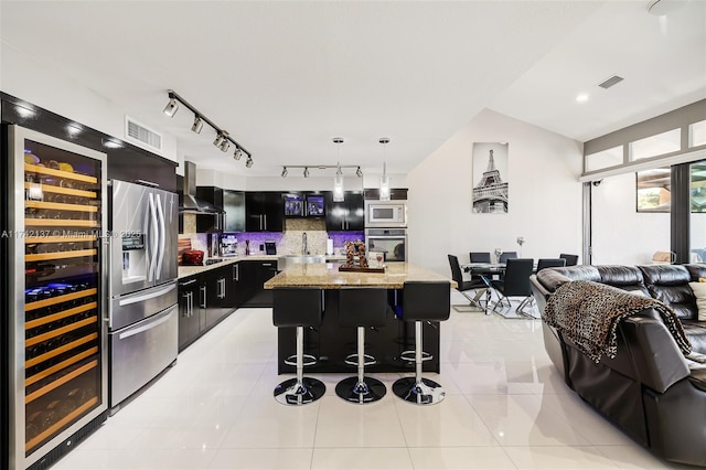 kitchen featuring wall chimney range hood, appliances with stainless steel finishes, hanging light fixtures, a kitchen breakfast bar, and a kitchen island