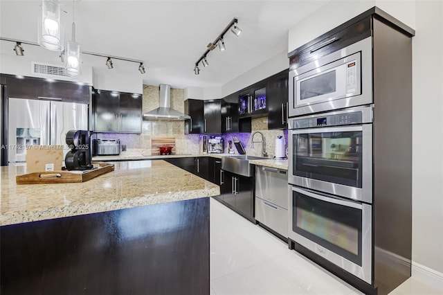 kitchen with sink, stainless steel appliances, decorative backsplash, decorative light fixtures, and wall chimney exhaust hood