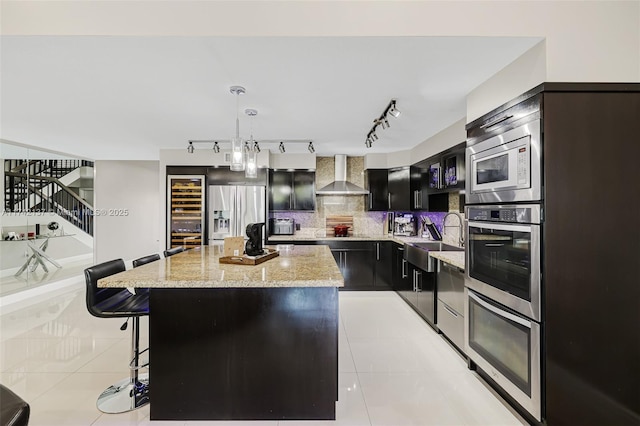 kitchen with appliances with stainless steel finishes, hanging light fixtures, a center island, light tile patterned floors, and wall chimney range hood