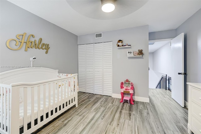 bedroom with ceiling fan, light hardwood / wood-style floors, a closet, and a nursery area