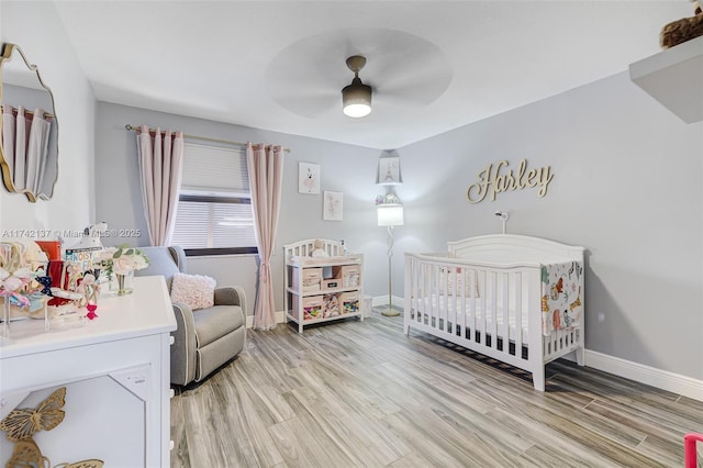 bedroom featuring a crib, light hardwood / wood-style floors, and ceiling fan