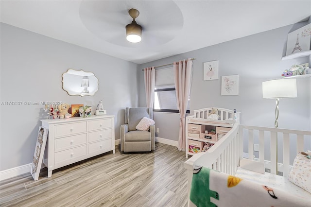 bedroom with a crib, light hardwood / wood-style floors, and ceiling fan