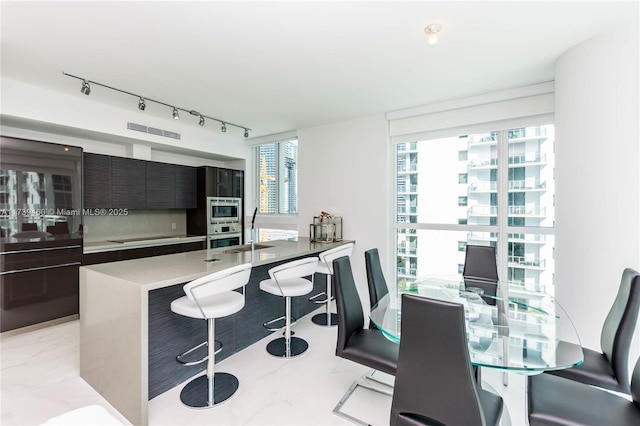 kitchen featuring a kitchen bar, sink, tasteful backsplash, dark brown cabinets, and appliances with stainless steel finishes