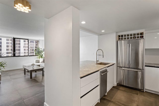 kitchen with an inviting chandelier, appliances with stainless steel finishes, sink, and white cabinets