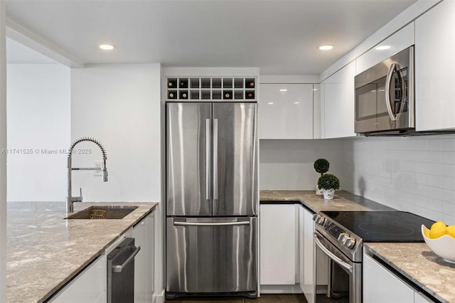 kitchen with sink, white cabinetry, stainless steel appliances, light stone countertops, and backsplash