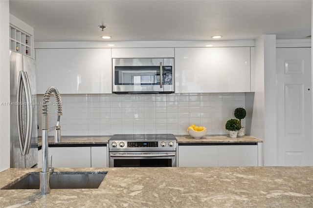 kitchen featuring sink, white cabinetry, stainless steel appliances, light stone countertops, and decorative backsplash