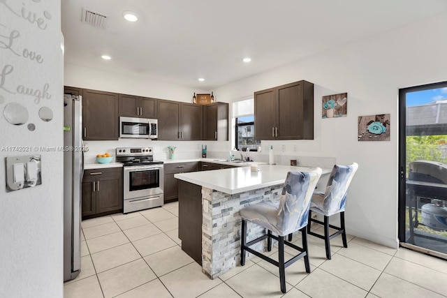 kitchen featuring appliances with stainless steel finishes, a breakfast bar area, light tile patterned floors, and kitchen peninsula