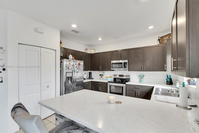 kitchen featuring a breakfast bar, sink, dark brown cabinetry, kitchen peninsula, and stainless steel appliances