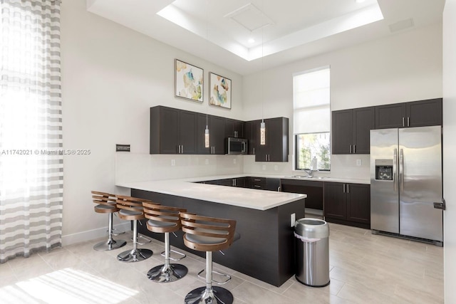 kitchen featuring sink, a tray ceiling, kitchen peninsula, a towering ceiling, and stainless steel appliances