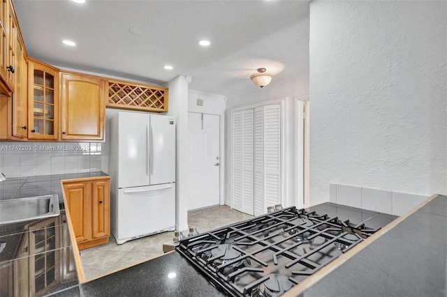 kitchen with sink, light tile patterned floors, tasteful backsplash, black gas stovetop, and white fridge