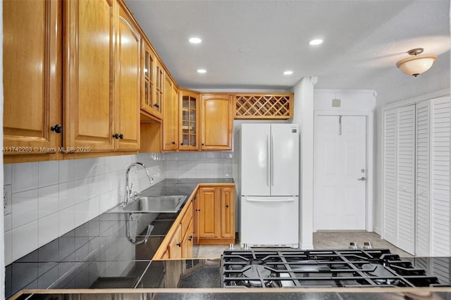 kitchen with decorative backsplash, freestanding refrigerator, a sink, and glass insert cabinets