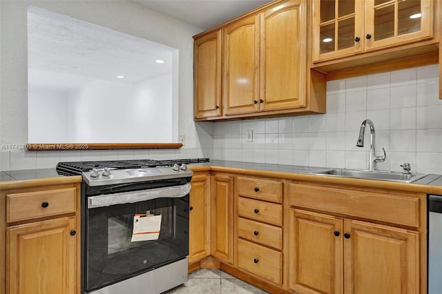 kitchen with tile counters, light tile patterned floors, a sink, glass insert cabinets, and appliances with stainless steel finishes