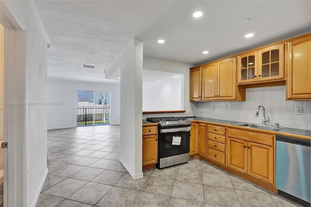 kitchen featuring stainless steel appliances, a sink, decorative backsplash, glass insert cabinets, and tile counters