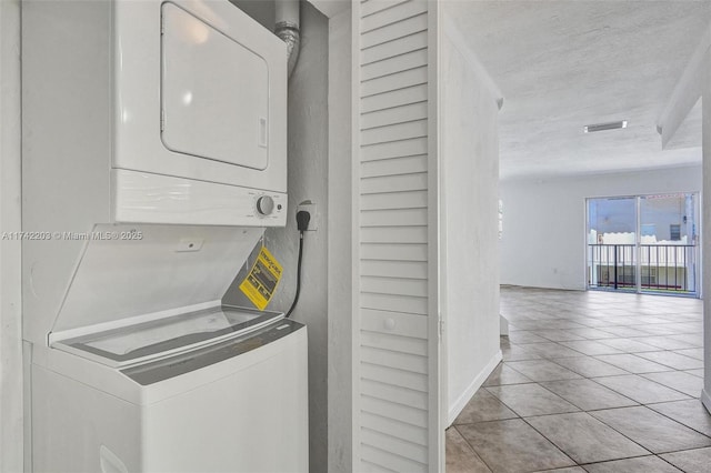 washroom featuring stacked washer / drying machine, laundry area, visible vents, light tile patterned flooring, and a textured ceiling