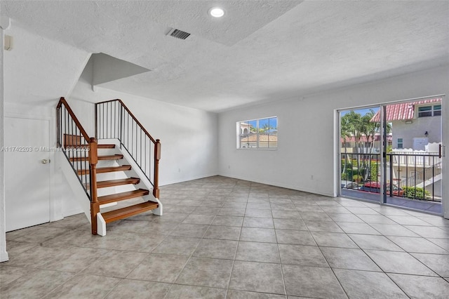 interior space featuring baseboards, tile patterned flooring, a textured ceiling, and visible vents