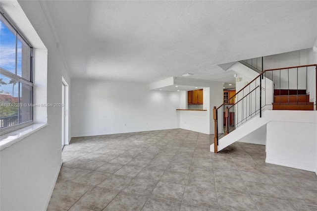unfurnished living room with baseboards, a textured ceiling, tile patterned floors, and stairs