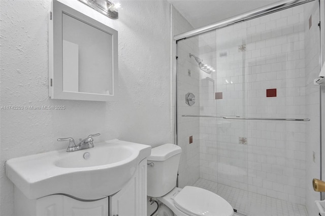 bathroom with toilet, a textured wall, vanity, and a stall shower