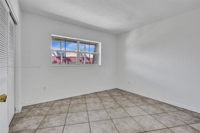 unfurnished room featuring baseboards, a textured ceiling, and light tile patterned floors