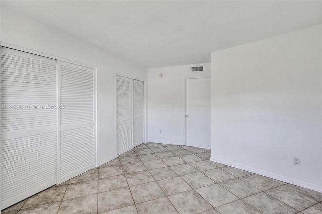 unfurnished bedroom with two closets, visible vents, and light tile patterned floors