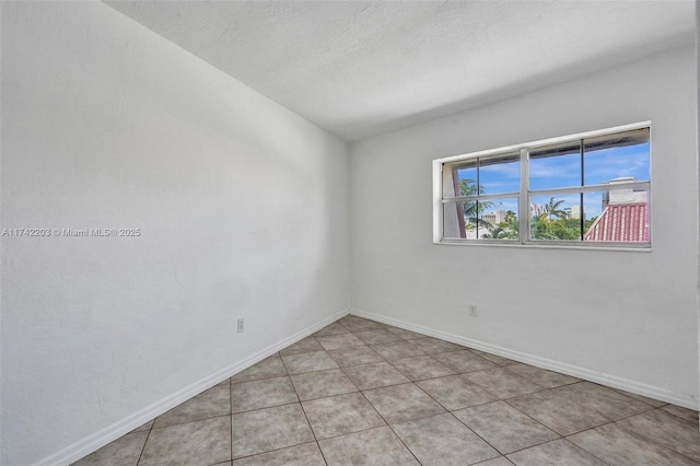 spare room featuring baseboards, a textured ceiling, and light tile patterned floors