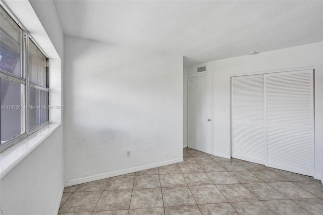 unfurnished bedroom featuring a closet, visible vents, baseboards, and light tile patterned floors