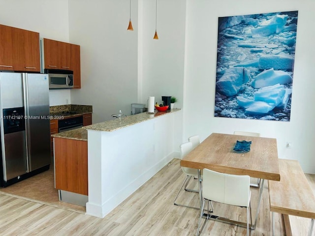 kitchen featuring stainless steel appliances, kitchen peninsula, hanging light fixtures, and light hardwood / wood-style flooring