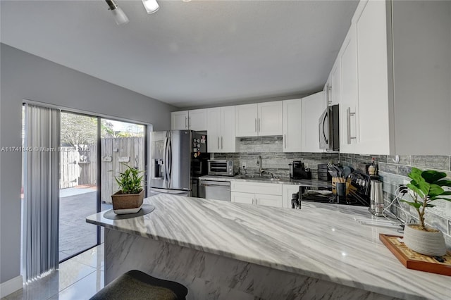 kitchen with sink, white cabinets, decorative backsplash, stainless steel appliances, and light stone countertops