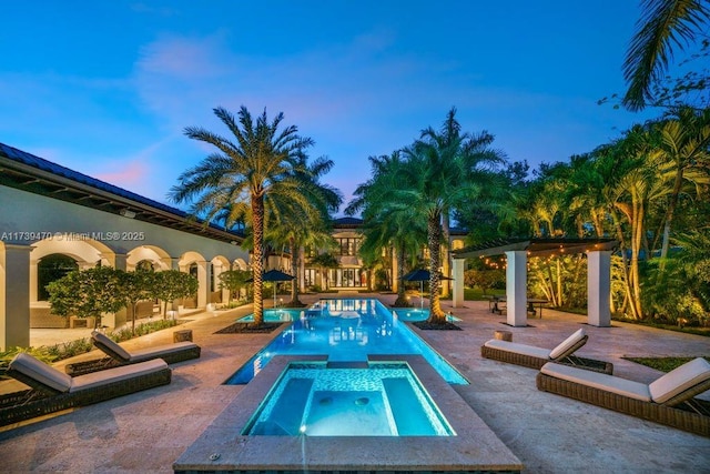 pool at dusk featuring a pergola, a patio area, and an in ground hot tub