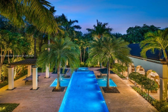 pool at dusk featuring pool water feature and a patio