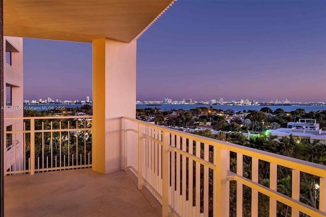 balcony at dusk featuring a water view and a city view