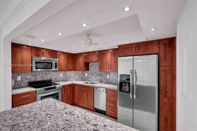 kitchen with a tray ceiling, sink, ceiling fan, light stone counters, and stainless steel appliances