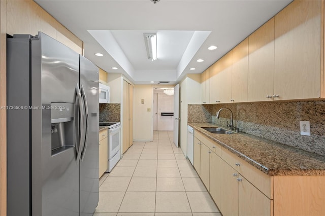 kitchen featuring sink, light tile patterned floors, a tray ceiling, white appliances, and dark stone counters