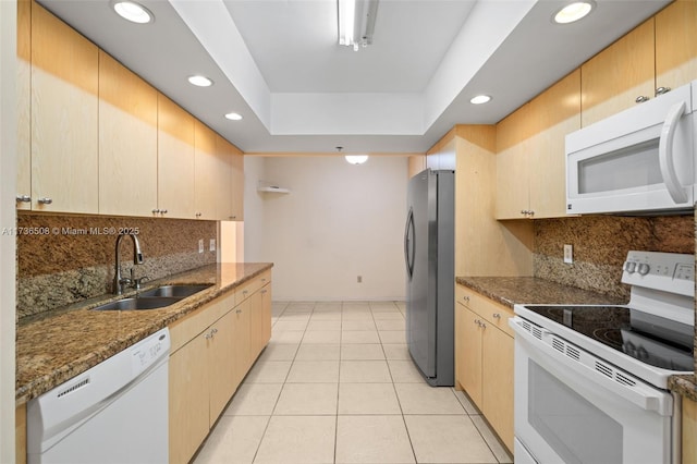 kitchen featuring sink, light tile patterned floors, dark stone countertops, a tray ceiling, and white appliances