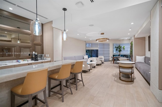 bar featuring light stone counters, decorative light fixtures, and light hardwood / wood-style flooring