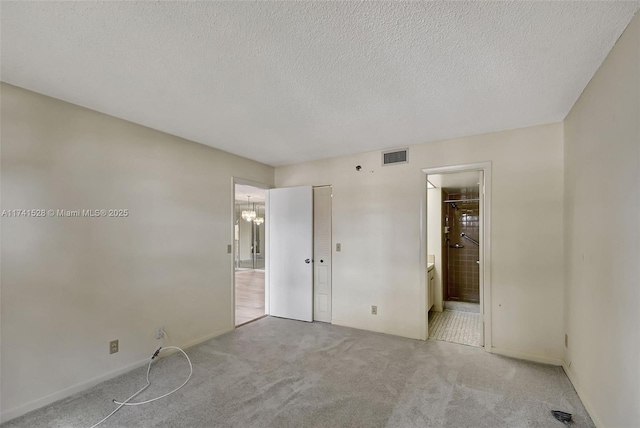 carpeted spare room with a chandelier, a textured ceiling, and ensuite bathroom