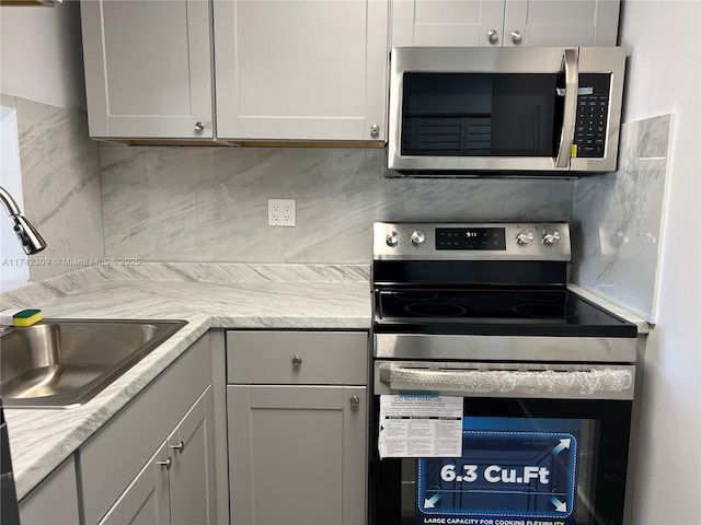 kitchen with backsplash, appliances with stainless steel finishes, sink, and gray cabinetry