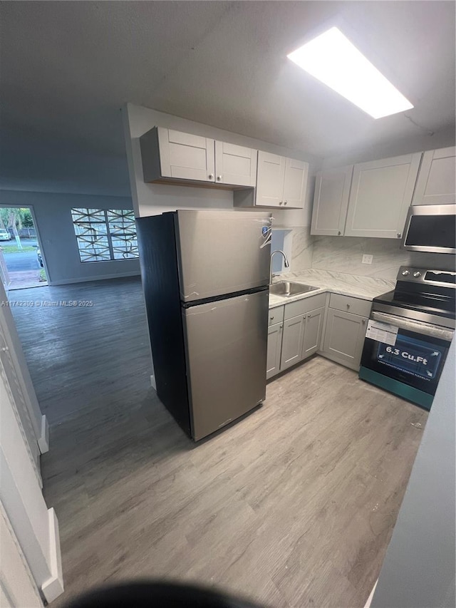 kitchen with appliances with stainless steel finishes, tasteful backsplash, sink, gray cabinetry, and light hardwood / wood-style flooring